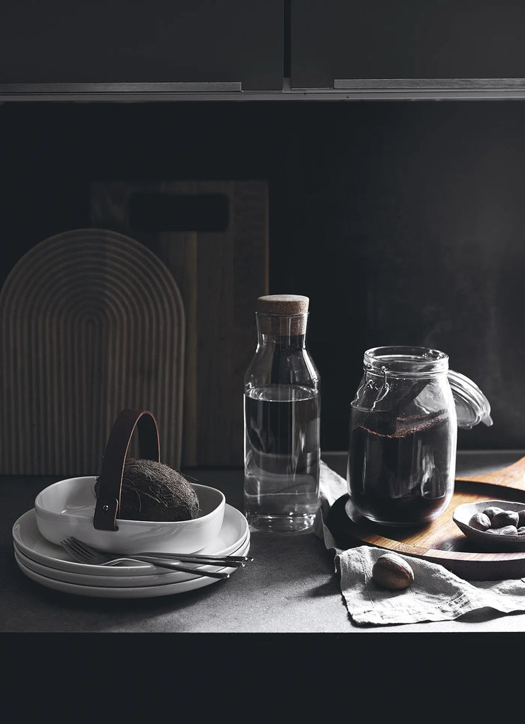 A black and white photo of a kitchen with a COZY coffee jar, plates and utensils.