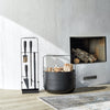 A black EMMA WOOD BASKET holder next to a fireplace. (Brand: ELDVARM)
