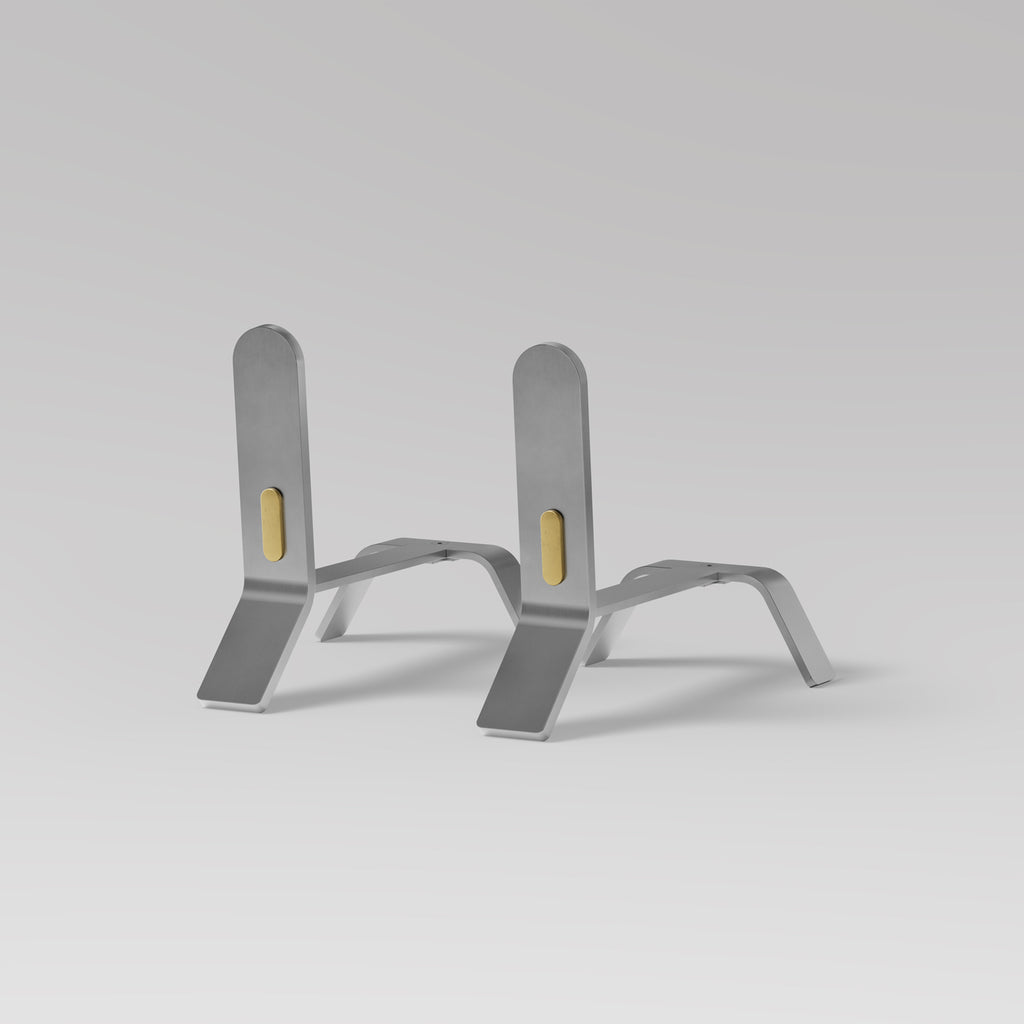 Introducing a minimalist design of Eldvarm Cooper Fire Dogs, featuring brass detail, elegantly holding up a stack of books on a grey background.