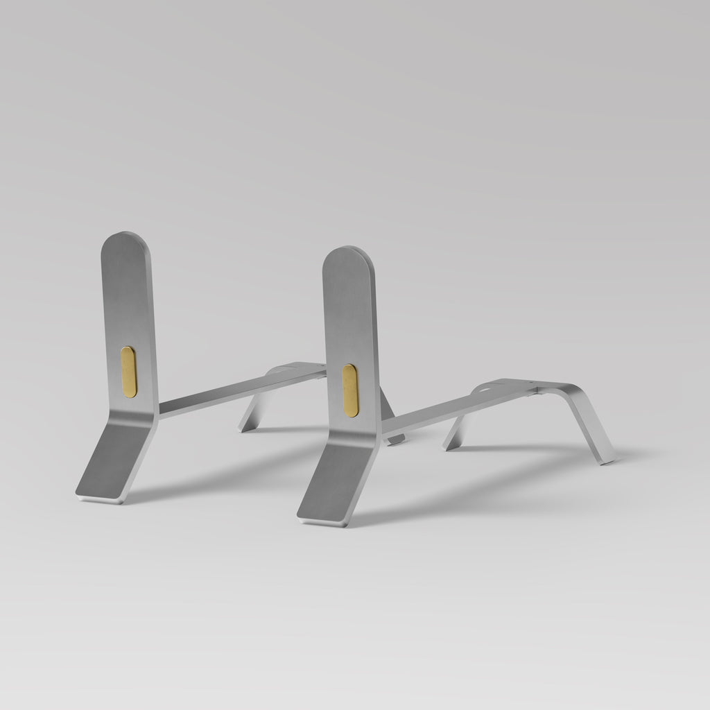 A pair of Eldvarm Cooper Fire Dogs, elegantly designed with a minimalist stainless steel finish, showcased against a serene grey background.