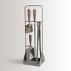 The ELDVARM EMMA FIRE TOOL COMPANION SET includes a brush, shovel, poker, and tongs with wooden handles, all displayed on a metal stand—perfect fireplace accessories.