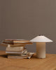 A small stack of worn books sits beside the minimalist FUTÉ Table Lamp, a fine example of LYFA's Danish design, on a wooden surface against a plain wall.