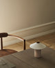A minimalist interior with a wooden chair and table showcases Danish design. The LYFA FUTÉ Table Lamp, small and white, sits on the table's corner. Neutral-toned walls and floor complete this elegant lighting arrangement.