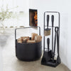 An EMMA FIRE TOOL COMPANION SET by ELDVARM black bucket with a firewood holder and a broom.