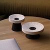 Two Origin Made Coliseu Pedestals on a wooden table.