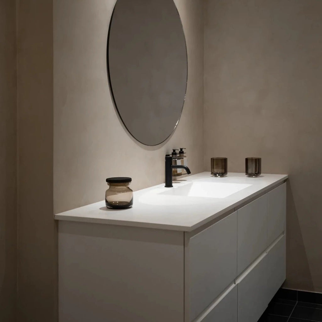 A white bathroom with a round mirror over the sink.